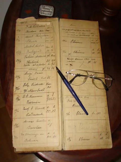 Handwritten order book open on a table, with a pen and reading glasses